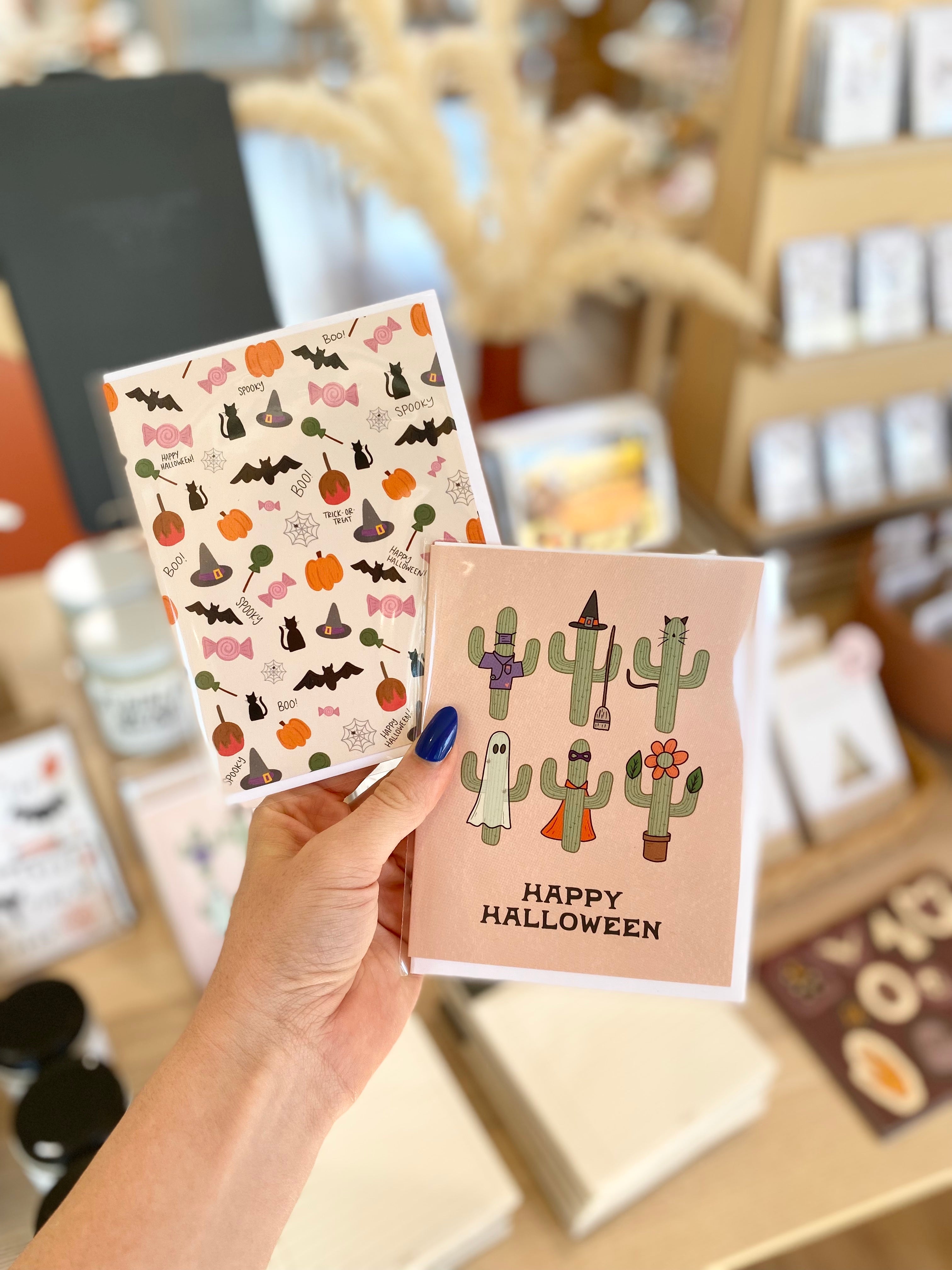 Cute and spooky and happy halloween cacti greeting cards being held over a table